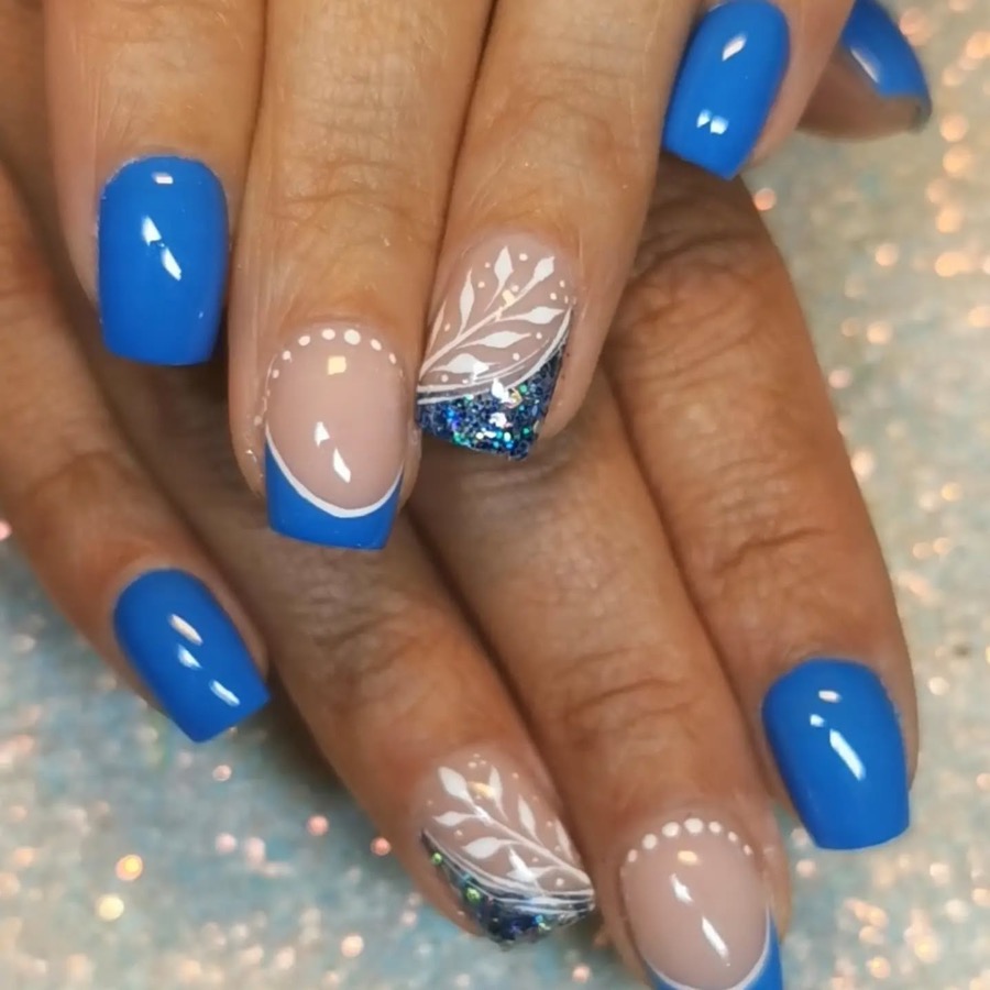 Ongles bleu roi, deux ongles nude à french bleue décorés de feuillage blanc et de paillettes